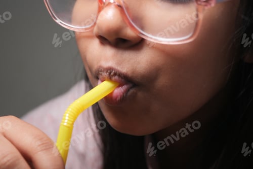 Preview: Young girl sipping a drink through a yellow straw at home