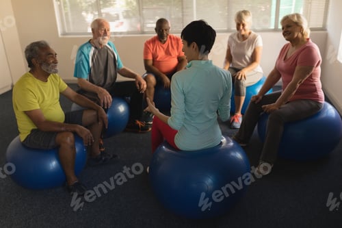 Preview: Front view of female trainer training senior people in performing exercise on ball at home
