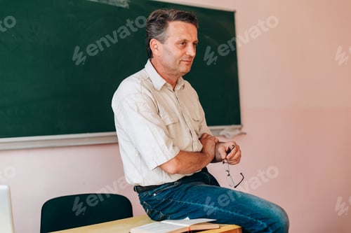 Preview: Smiling middle age teacher sitting at the table and explain the lesson .- Image