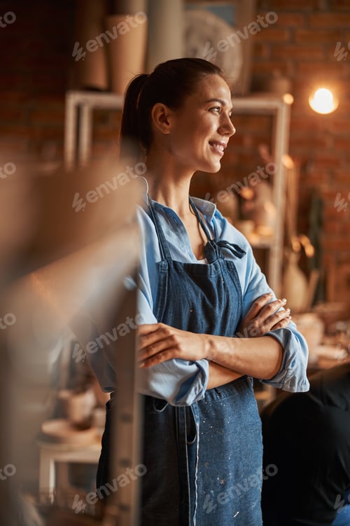 Preview: Beautiful brunette Caucasian craft woman wearing apron looking away in art studio