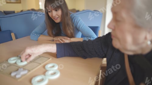 Preview: Young woman watches senior play tic-tac-toe