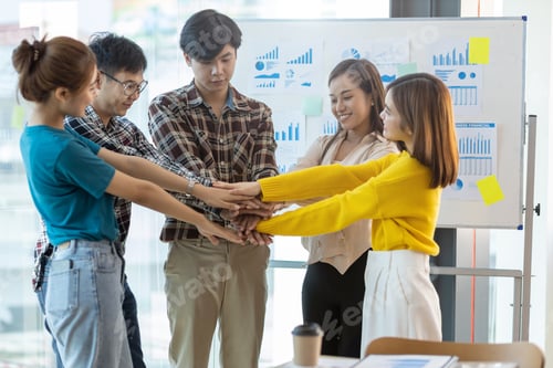 Preview: Group young business people putting their hands together in the office. Unity and teamwork concept.