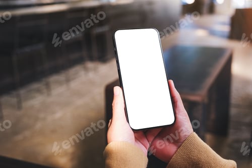 Preview: Mockup image of a woman holding and using mobile phone with blank desktop in cafe