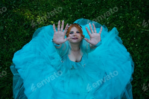 Preview: Top view of redhead young bride with acne in blue dress in park raising her hands to camera.