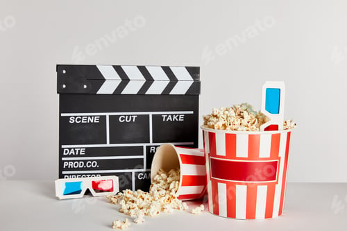 Preview: delicious popcorn scattered from buckets with clapper board and 3d glasses isolated on grey