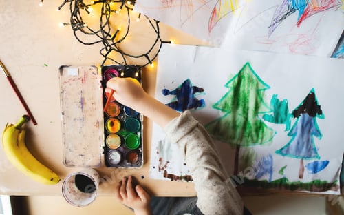 Preview: Top view of unrecognizable small child indoors at home at Christmas, painting pictures