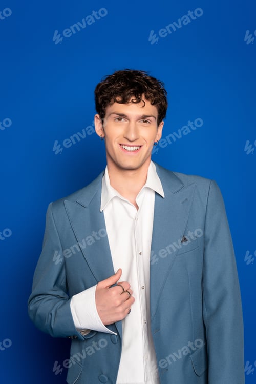 Preview: Portrait of curly man in jacket and shirt looking at camera on blue background