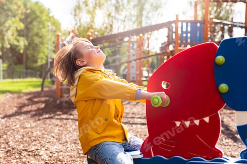 Preview: Preschool boy on children playground, happy emotional child swinging on teeterboard in a park.