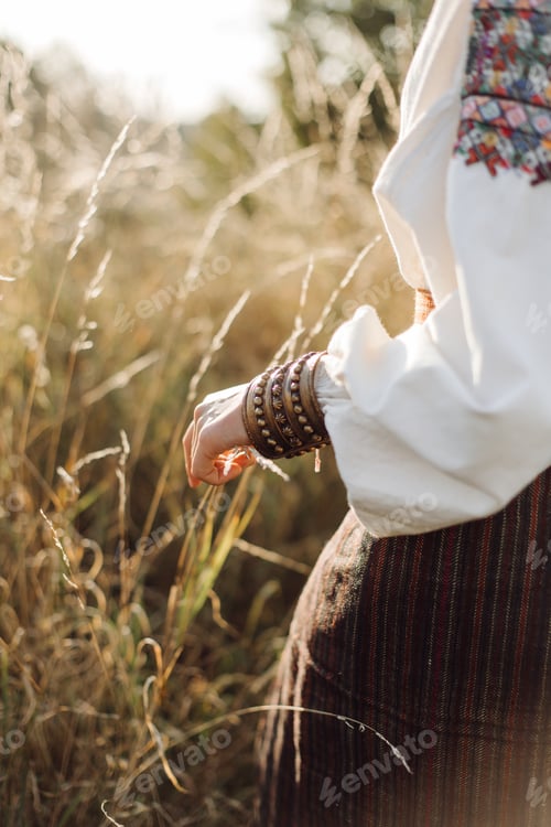 Preview: Young woman in traditional national embroidered shirt and skirt on nature at sunset.
