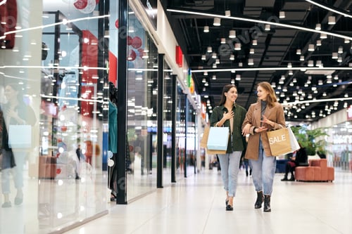 Preview: Two young contemporary females in elegant casualwear walking along shopwindows