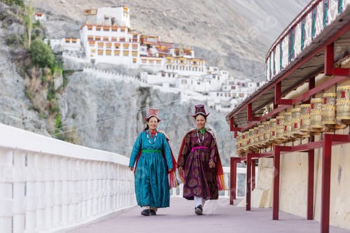 Preview: Two women in vibrant traditional attire walk past prayer wheels at a monastery in Nubra Valley