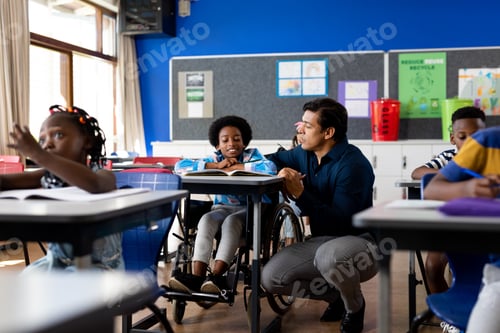 Preview: Biracial male teacher helping schoolboy sitting in wheelchair in classroom at elementary school