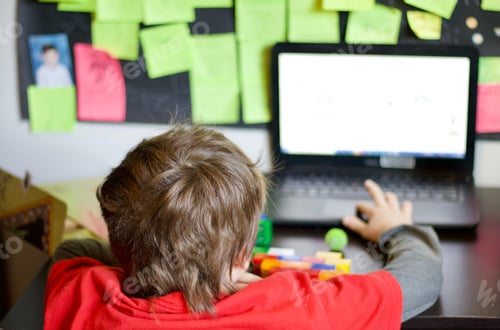 Preview: Boy using laptop for schoolwork during online virtual school during coronavirus with messy desk