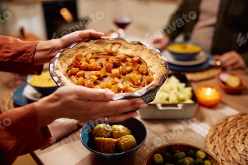 Preview: Close up of woman serving pumpkin pie during Thanksgiving dinner at home.
