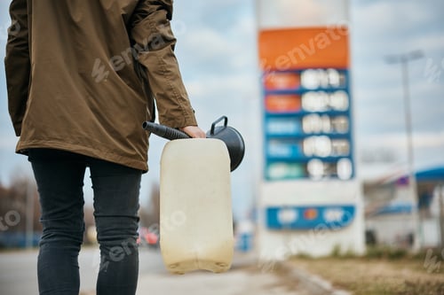 Preview: Unrecognizable woman carrying plastic gallon while walking to gas station.