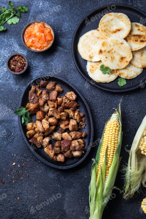 Preview: COLOMBIAN FOOD. Maize AREPAS and fried pork chicharron ans colombian tomato sauce. Top view. Black