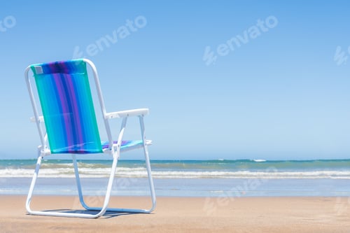 Preview: Colorful deckchair with thermos and matte on the sand overlookin