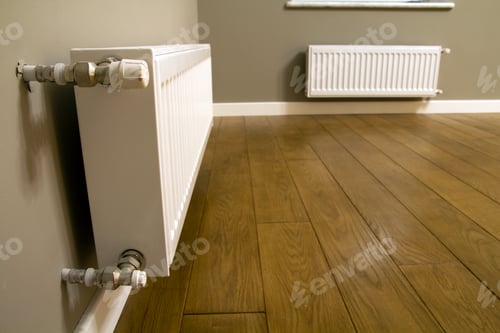Preview: White metal heating radiator mounted on gray wall inside a room.