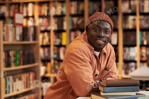 Preview: Portrait of Young Black Man Smiling While Leaning on Stack of Books
