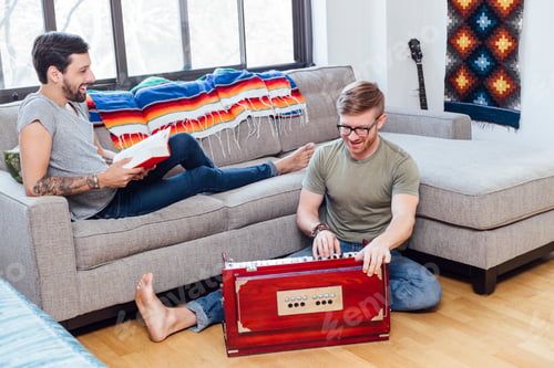 Preview: Male couple at home, Young man on sofa watching his partner play musical instrument