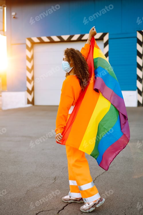 Preview: African American lesbian woman with medical face mask posing with lgbt pride flag. Covid-19.