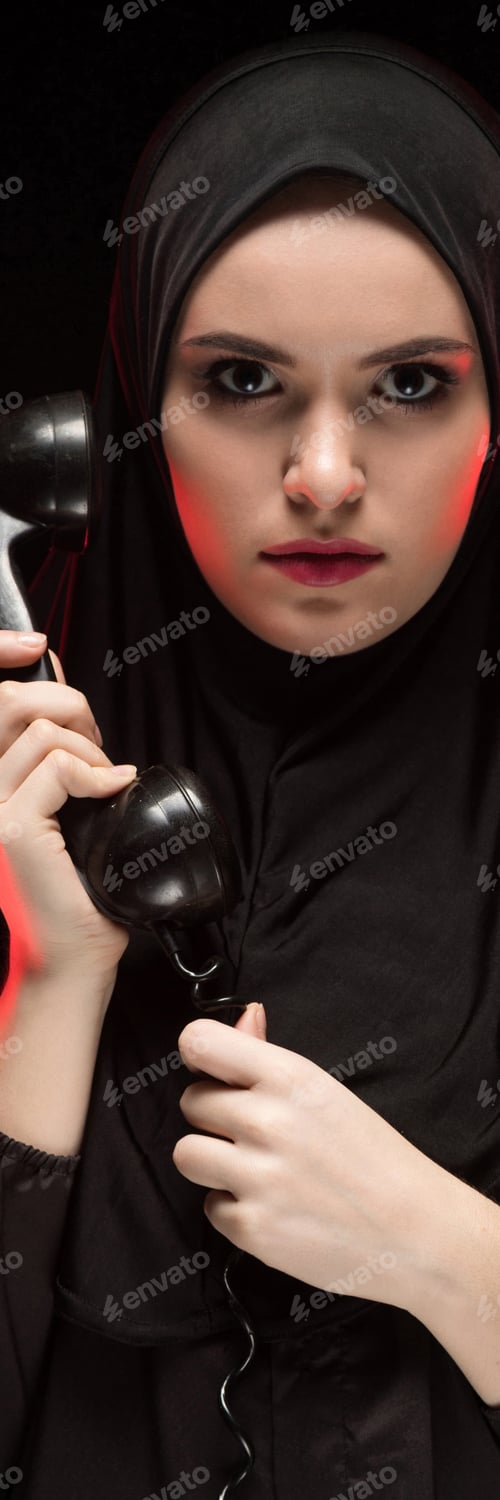 Preview: Portrait of beautiful serious scared young muslim woman wearing black hijab holding telephone to