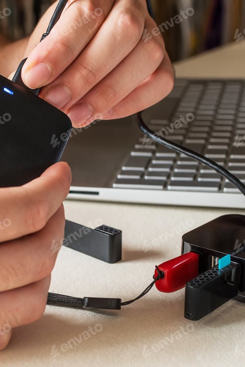 Preview: Male hand connecting the hard drive with a USB cable to a laptop computer and USB splitter device