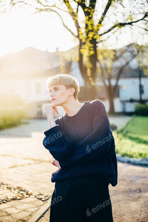Preview: Fashion portrait of a stylish woman in an oversized sweater outdoors in the rays of the setting sun.