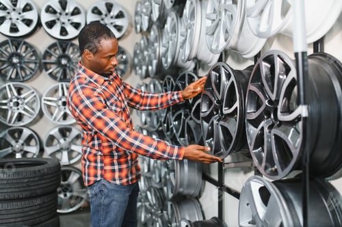 Preview: African american Car mechanic holding car rims ready to mount the wheels in workshop