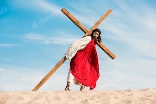 Preview: jesus walking with wooden cross in desert against sky