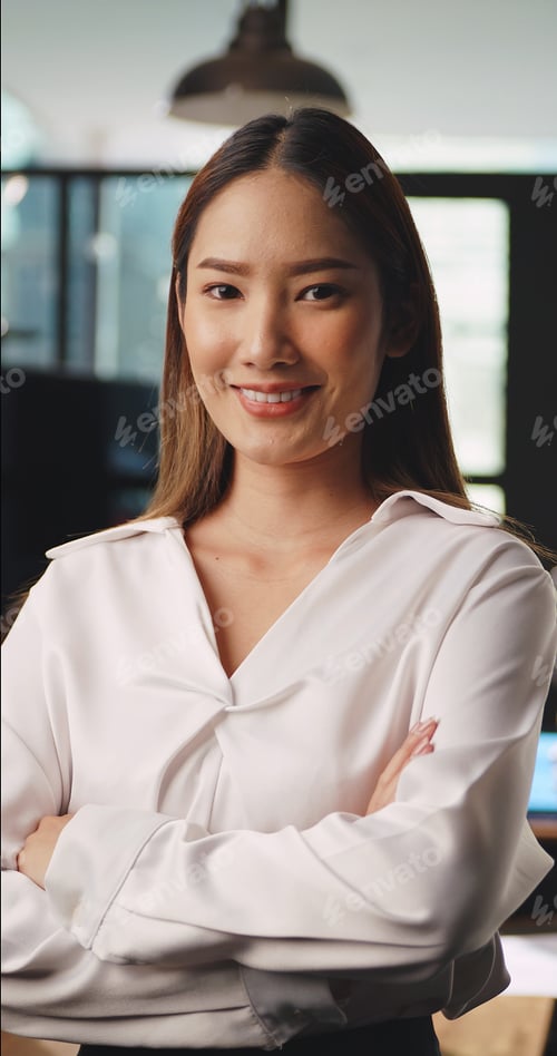 Preview: Portrait of young beautiful businesswoman standing with arms crossed looking at camera in office.