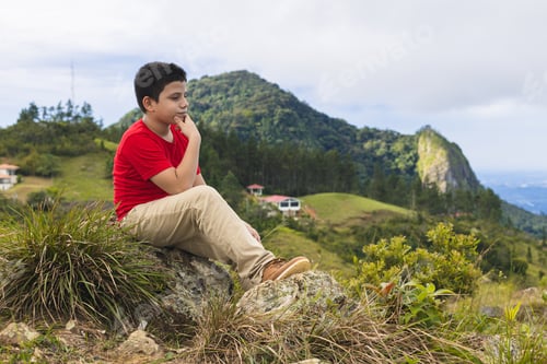 Preview: latin boy sitting thinking on the mountain
