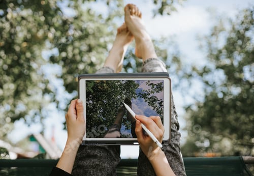 Preview: Teenage girl sits in the garden on a swing upside down and draws sketches on a tablet