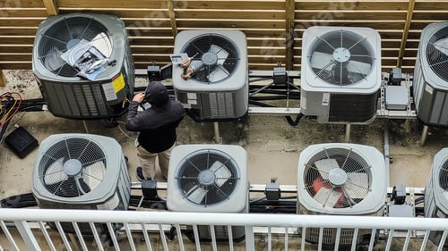 Preview: Overhead shot HVAC technician servicing group of condo Air conditioners electrical in fenced area.