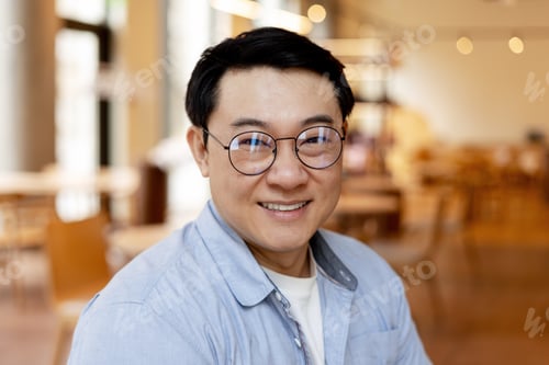 Preview: Asian manager smiling wearing glasses in modern office cafeteria