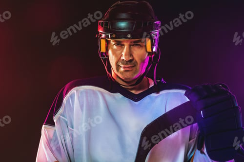Preview: Male hockey player with the stick on ice court and dark neon colored background
