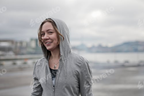 Preview: Portrait of young female runner wearing hoody on windy dockside
