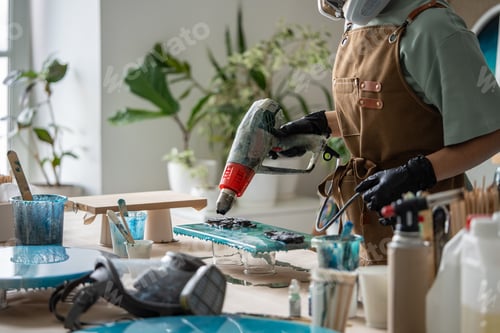 Preview: Artist use hot air gun clear excess epoxy resin from painting in creative workshop, flawless artwork