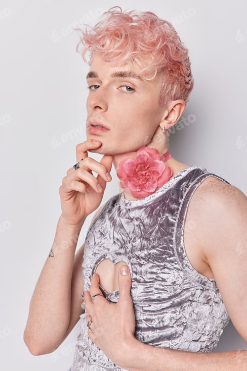 Preview: Young queer man stands in profile has muscular arms wears silver t shirt looks directly at camera