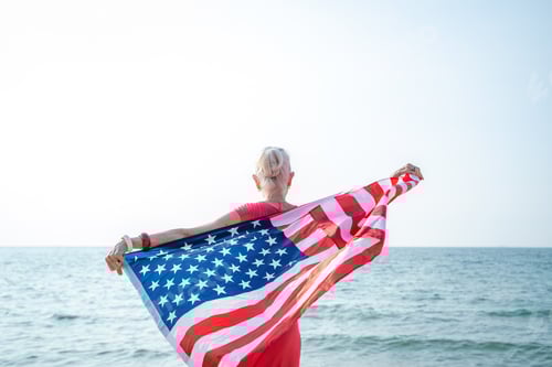 Preview: Mature woman holding US flag enjoying time at the beach.