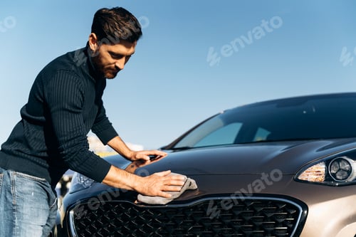 Preview: Low angle shot of a happy young man polishing his car with microfiber cloth