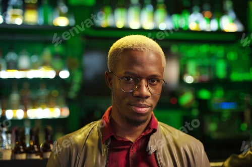 Preview: Young African man in smart casualwear and eyeglasses standing against bar