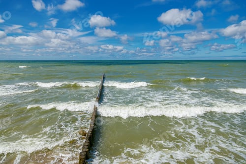 Preview: Waves of the Baltic sea breaking on a wooden groynes under a bright blue sky