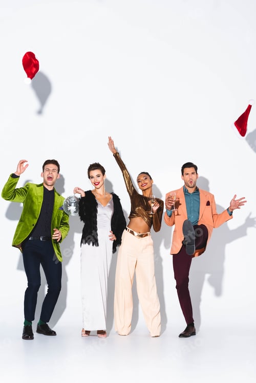 Preview: happy and stylish multicultural friends throwing in air santa hats and holding champagne glasses on