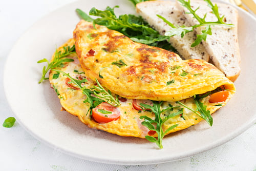 Aperçu: Omelette with tomatoes, ham, cheese and green herbs on plate. Frittata - italian omelet.