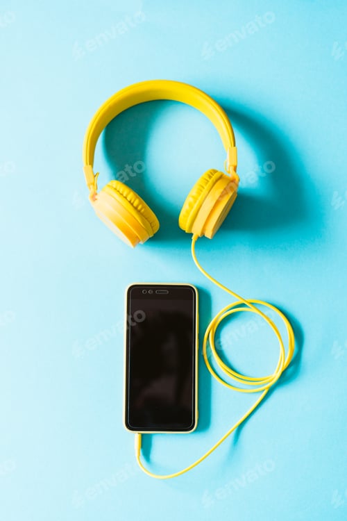 Preview: top view of yellow headset and mobile phone over blue background. Modern technology