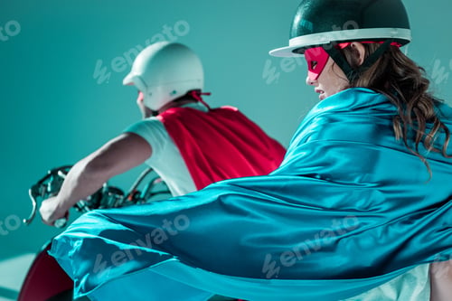 Preview: selective focus of couple in helmets and superhero capes on scooter
