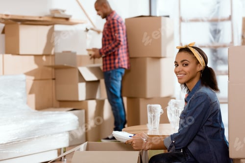 Preview: smiling african american girl unpacking dishware in new home