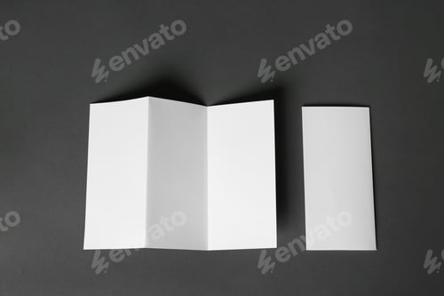 Preview: Two blank brochures on dark grey background, flat lay. Mock up for design