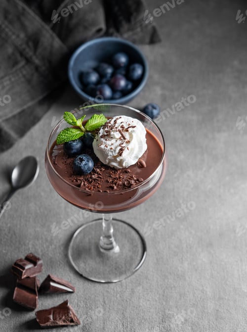 Preview: Chocolate pudding in a glass with whipped cream, fresh blueberries and mint on a dark background
